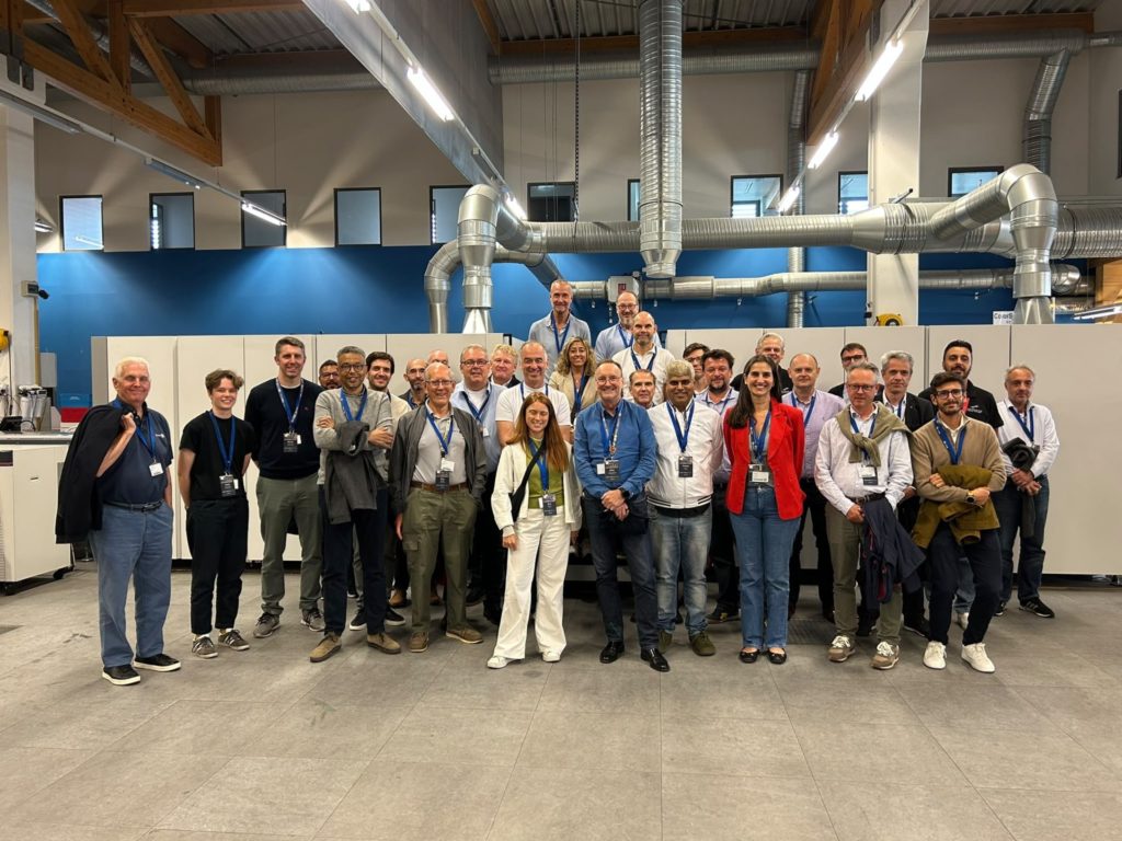 Photo de groupe des visiteurs rassemblés devant une grande imprimante